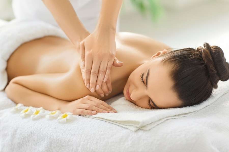 Une femme détendue reçoit un massage suédois apaisant sur le dos dans un spa lumineux.